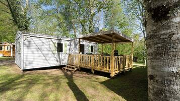 A mobile home with a porch and a covered area, surrounded by trees.