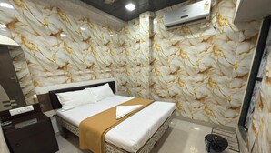 Una habitación de hotel con pared de diseño de mármol, cama con ropa blanca y un plaid marrón, una mesita de noche y un equipo de aire acondicionado.