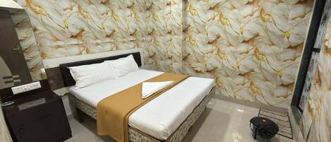 A hotel room with a marble-patterned wall, a bed with white linens and a brown throw, a nightstand, and an air conditioning unit.