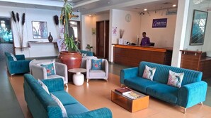 Een hotel lobby met blauwgroene banken, een receptiebalie en een grote potplant.