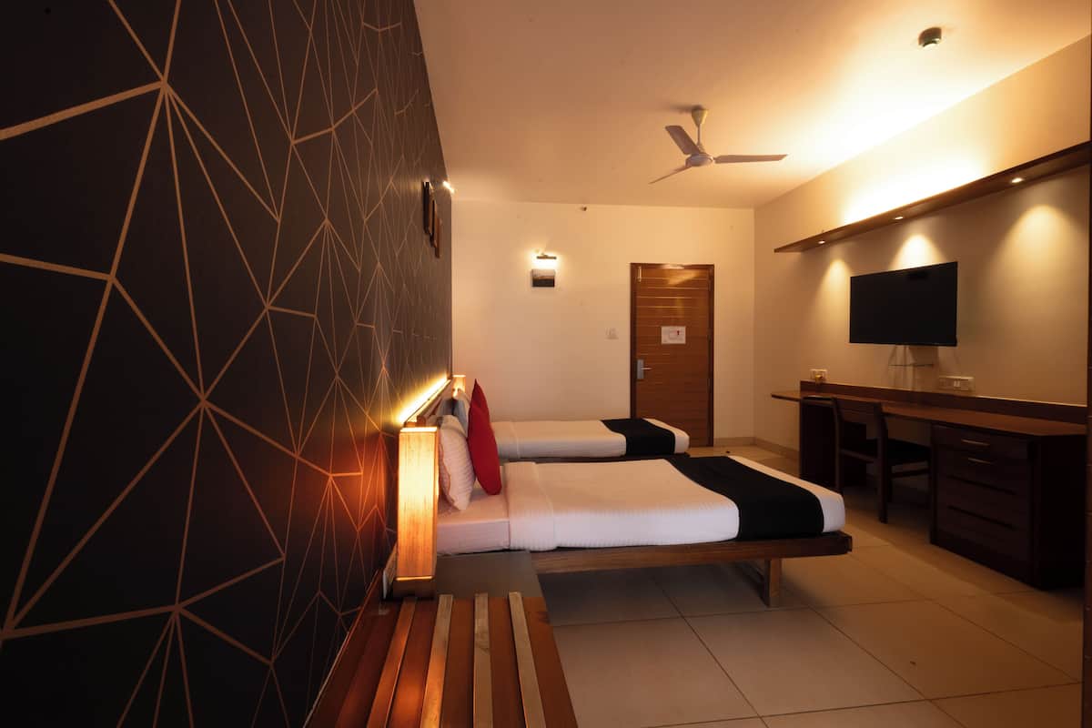 Ein Hotelzimmer mit zwei Betten, einem Schreibtisch, einem Fernseher und einem Deckenventilator.