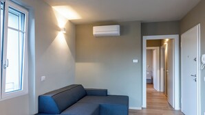 Een moderne woonkamer met een hoekbank, een luchtverwarmingssysteem aan het plafond en een gang naar andere ruimtes.