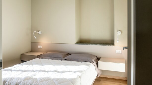 Een slaapkamer met een bed, nachtkastjes, een wandplank en een lamp.
