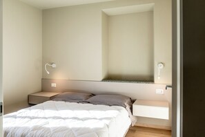 A bedroom with a bed, bedside tables, a wall-mounted shelf, and a light fixture.
