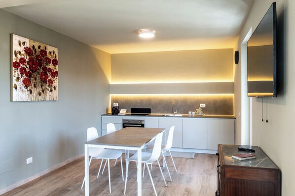 A modern kitchen with white cabinetry, a wooden dining table, and a large painting on the wall.