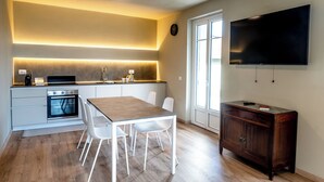 Een moderne keuken met een eethoek, inbouwoven, witte stoelen en een flatscreen televisie aan de muur.