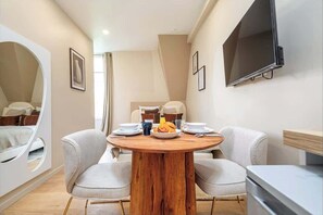 A modern room with a round wooden table set for breakfast, two chairs, a bed with a unique curved design, and a flat-screen TV mounted on the wall. - Studio Climatisé au Coeur de Paris - Pereire (Paris)