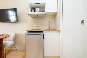 A compact kitchen with a built-in dishwasher, a small countertop, and a wall-mounted TV. - Studio Climatisé au Coeur de Paris - Pereire (Paris)