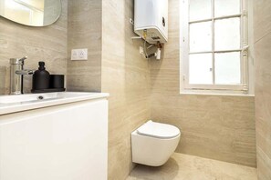 A bathroom with a white sink, a toilet, and a window. - Studio Climatisé au Coeur de Paris - Pereire (Paris)
