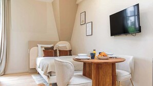 Moderni hotellihuone, jossa on sänky, ruokailutila pöytineen ja tuoleineen, seinälle asennettu taulutelevisio ja ikkuna, jossa on verhot.