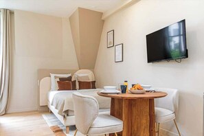 A modern hotel room with a bed, a dining area with a table and chairs, a flat-screen TV mounted on the wall, and a window with curtains. - Studio Climatisé au Coeur de Paris - Pereire (Paris)