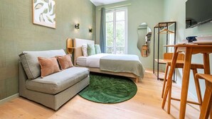 A compact room with a bed, a sofa, a dining table with chairs, a green rug, and a window with curtains. - Bright, air-conditioned studio for 2 people (Paris)