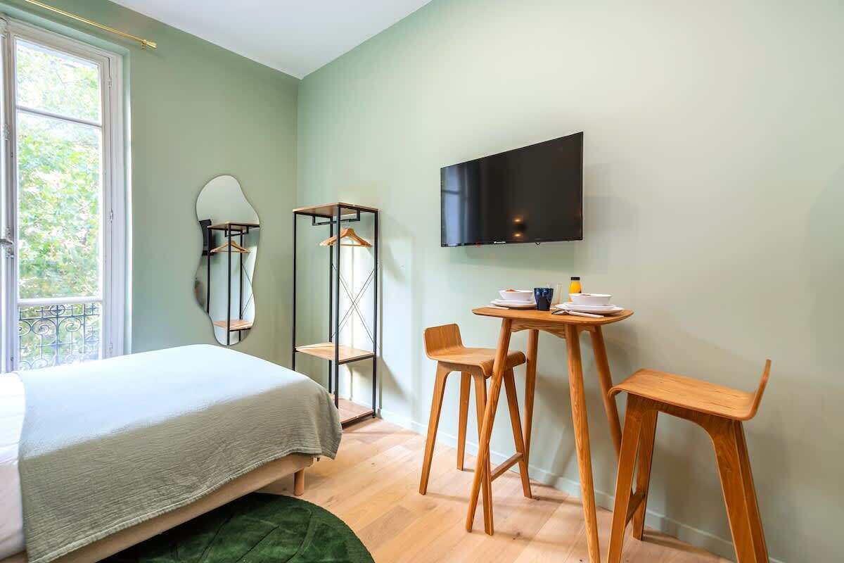 Een slaapkamer met een bed, een bureau met stoelen, een spiegel en een televisie aan de muur.