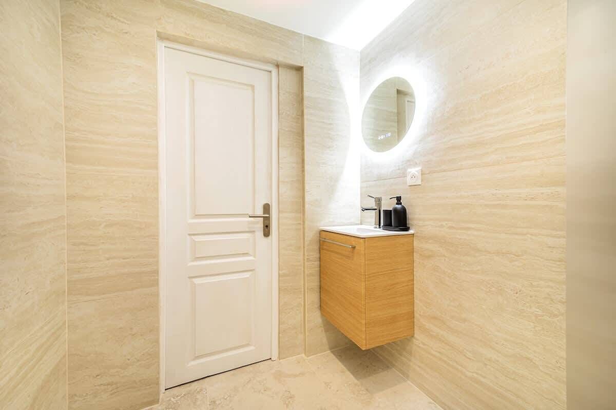 Une salle de bain avec une porte blanche, un meuble-lavabo en bois avec un miroir et un luminaire fixé au mur.