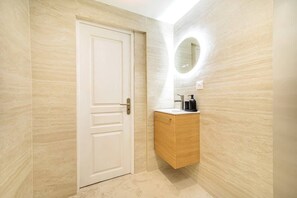 A bathroom with a white door, a wooden vanity with a mirror, and a light fixture on the wall. - Bright, air-conditioned studio for 2 people (Paris)