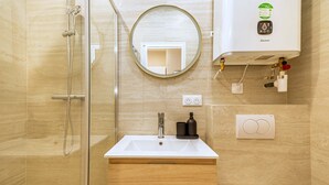 A bathroom with a glass-enclosed shower, a sink with a mirror above it, and a wall-mounted toilet. - Studio cosy et bien agencé - Pereire (Paris)