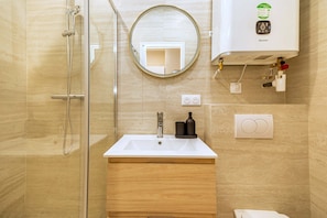 Ein Badezimmer mit einer Duschkabine, einem Waschbecken mit Spiegel darüber und einem an der Wand befestigten WC.