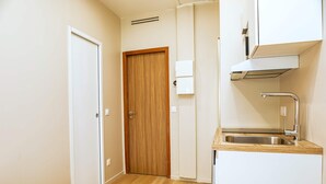 A small kitchenette with a wooden door, a white cabinet, a stainless steel sink, and a built-in range hood. - Studio cosy et bien agencé - Pereire (Paris)