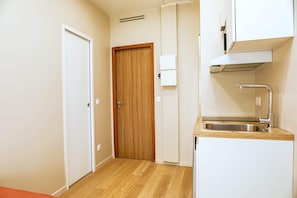 Eine kleine Küchenzeile mit einer Holztür, einem weißen Schrank, einer Edelstahlspüle und einer eingebauten Dunstabzugshaube.