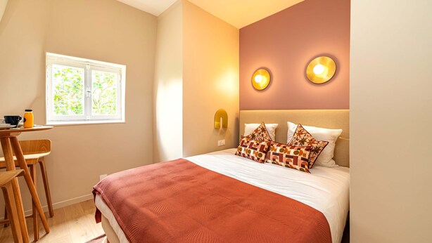 A bedroom with a bed, two wall-mounted lights, a window, and a desk with a chair. - Studio cosy et bien agencé - Pereire (Paris)
