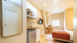 A compact bedroom with a bed, a small kitchenette, a TV, and a window. - Studio cosy et bien agencé - Pereire (Paris)