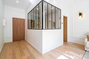 A room with a wooden door, a glass partition, and a white wall with a light fixture. - Elegant 2-room air-conditioned apartment - Paris 17 (Paris)