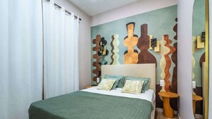 Ein Schlafzimmer mit einem Bett, Kissen, einer Wand mit abstrakter Kunst, einem Spiegel und Holzboden.