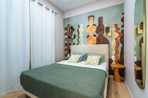 A bedroom with a bed, pillows, a wall with abstract art, a mirror, and a wooden floor. - Elegant 2-room air-conditioned apartment - Paris 17 (Paris)
