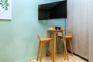 Ein Zimmer mit einem an der Wand befestigten Flachbildfernseher, einem kleinen Holztisch mit zwei Stühlen und einem Teller mit Donuts.
