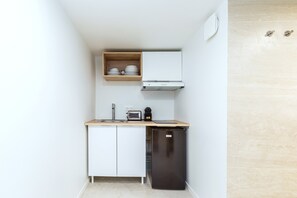 Eine kleine Küche mit weißen Schränken, einer Holz Arbeitsplatte, einem schwarzen Kühlschrank und einer eingebauten Ablage mit Geschirr.