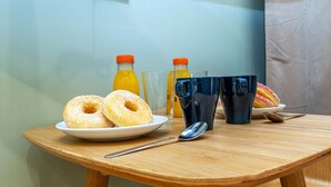 Et morgenbord med to donuts, to glas, to appelsinjuiceflasker, en sort kop, en ske og en tallerken med en donut.