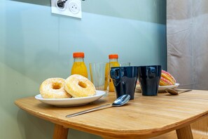 Ein Frühstückstisch mit zwei Donuts, zwei Gläsern, zwei Orangensaftflaschen, einer schwarzen Tasse, einem Löffel und einem Teller mit einem Donut.