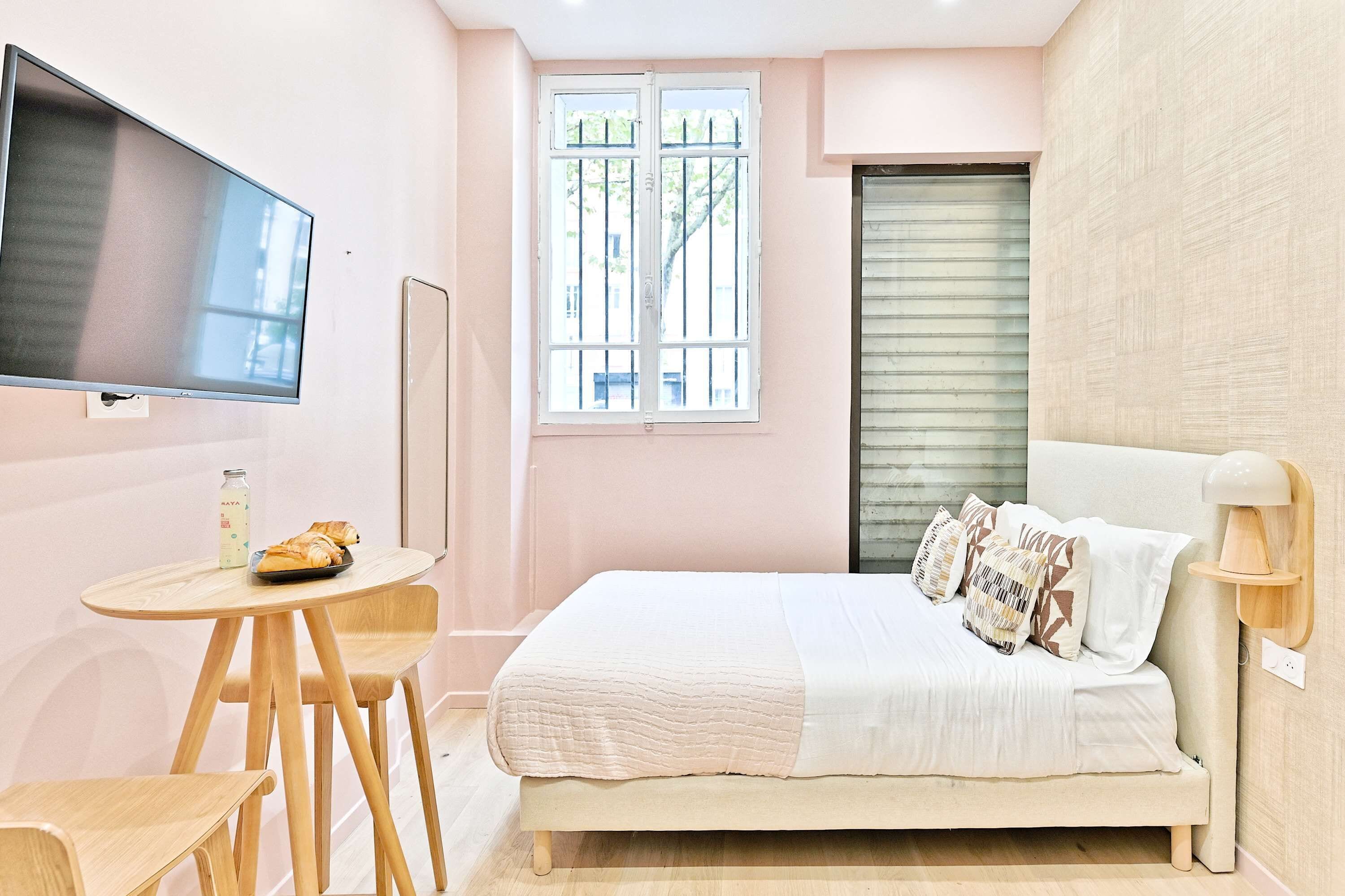 Un dormitorio con cama, televisor, ventana y una mesita con pasteles.