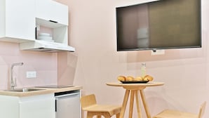 A kitchenette with a built-in oven, a sink, and a small dining area with two chairs and a table. - Studio climatisé, calme & tout équipé – Paris 17 (Paris)