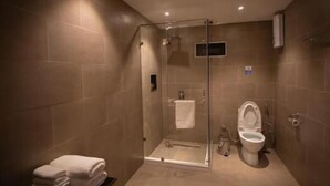 A modern bathroom with a glass-enclosed shower, a toilet, and a stack of towels on a shelf. - Nangter Retreat (Paro)
