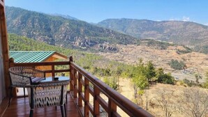Μια ξύλινη βεράντα με ένα τραπέζι και καρέκλες, από την οποία διακρίνεται ένα ορεινό τοπίο.