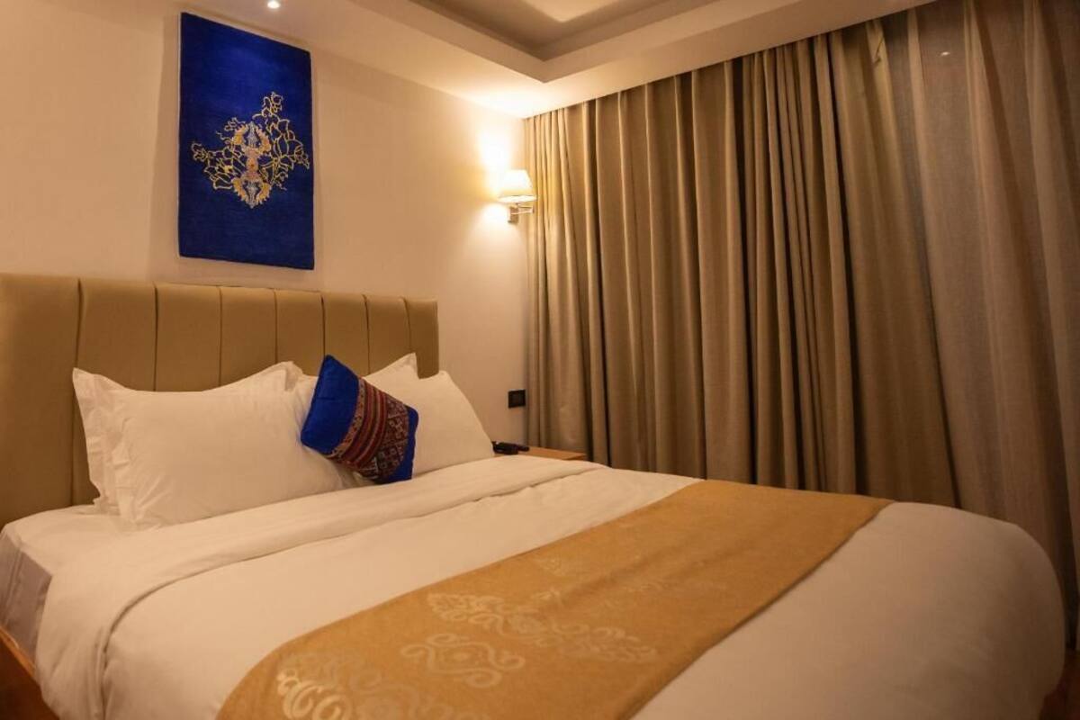 Une chambre d’hôtel avec un grand lit, des rideaux de couleur beige et une lampe fixée au mur.