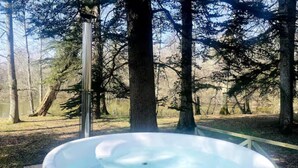 Un bain à remous situé dans un espace boisé, avec une terrasse en bois et une rambarde en métal.
