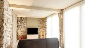 A modern living room with a stone wall, a flat-screen TV, and a dark-colored sofa. - Lake Orta elegant apartment. Vacation Lake Friends (Alzo)