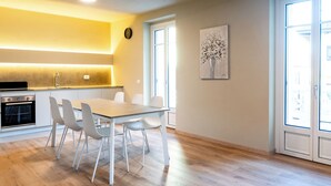 A modern kitchen with white cabinetry, a built-in oven, and a dining area with a wooden table and white chairs. - Lake Orta elegant apartment. Vacation Lake Friends (Alzo)