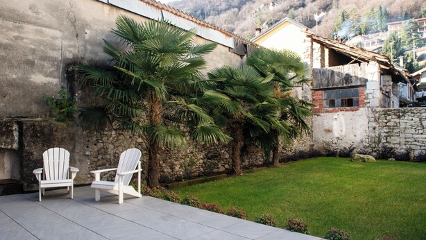 A patio with two white Adirondack chairs, a stone wall, and a grassy area. - Lake Orta elegant apartment. Vacation Lake Friends (Alzo)