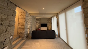 A modern interior with stone walls, a black sofa, and a flat-screen TV. - Lake Orta elegant apartment. Vacation Lake Friends (Alzo)