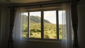 Ein Zimmer mit einem Bett, einem Deckenventilator und einem großen Fenster mit Vorhängen.