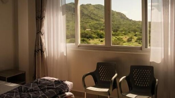 Ein Zimmer mit einem Bett, zwei Stühlen und einem Fenster mit Blick auf grüne Hügel.