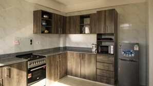 Eine Küche mit dunklen Holzausziehtüren, einer eingebauten Mikrowelle, einem Edelstahlkühlschrank und einem Gasherd.