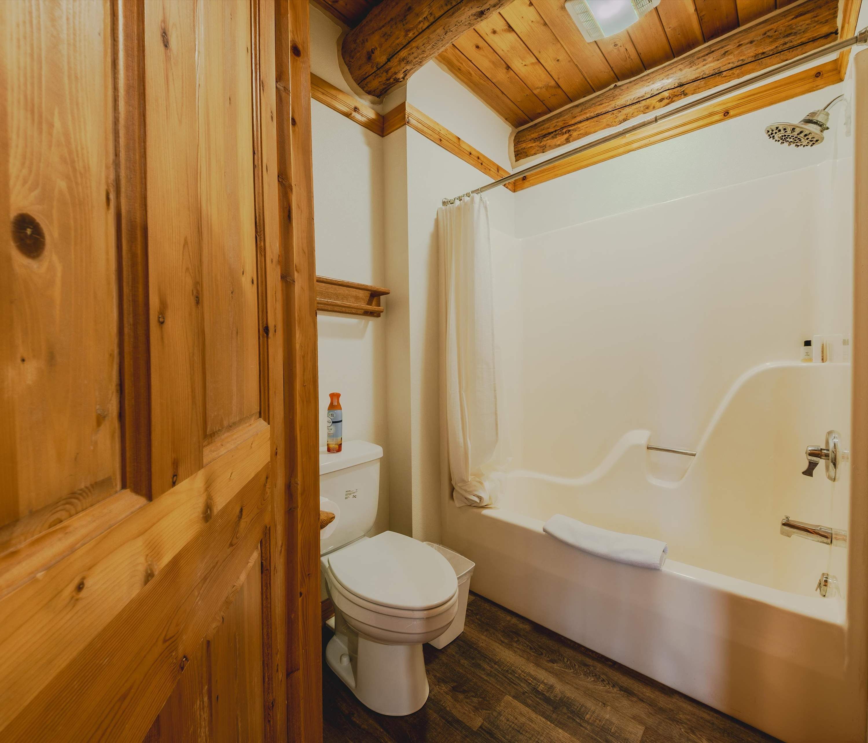 A wooden-paneled bathroom with a toilet, a bathtub, and a shower.