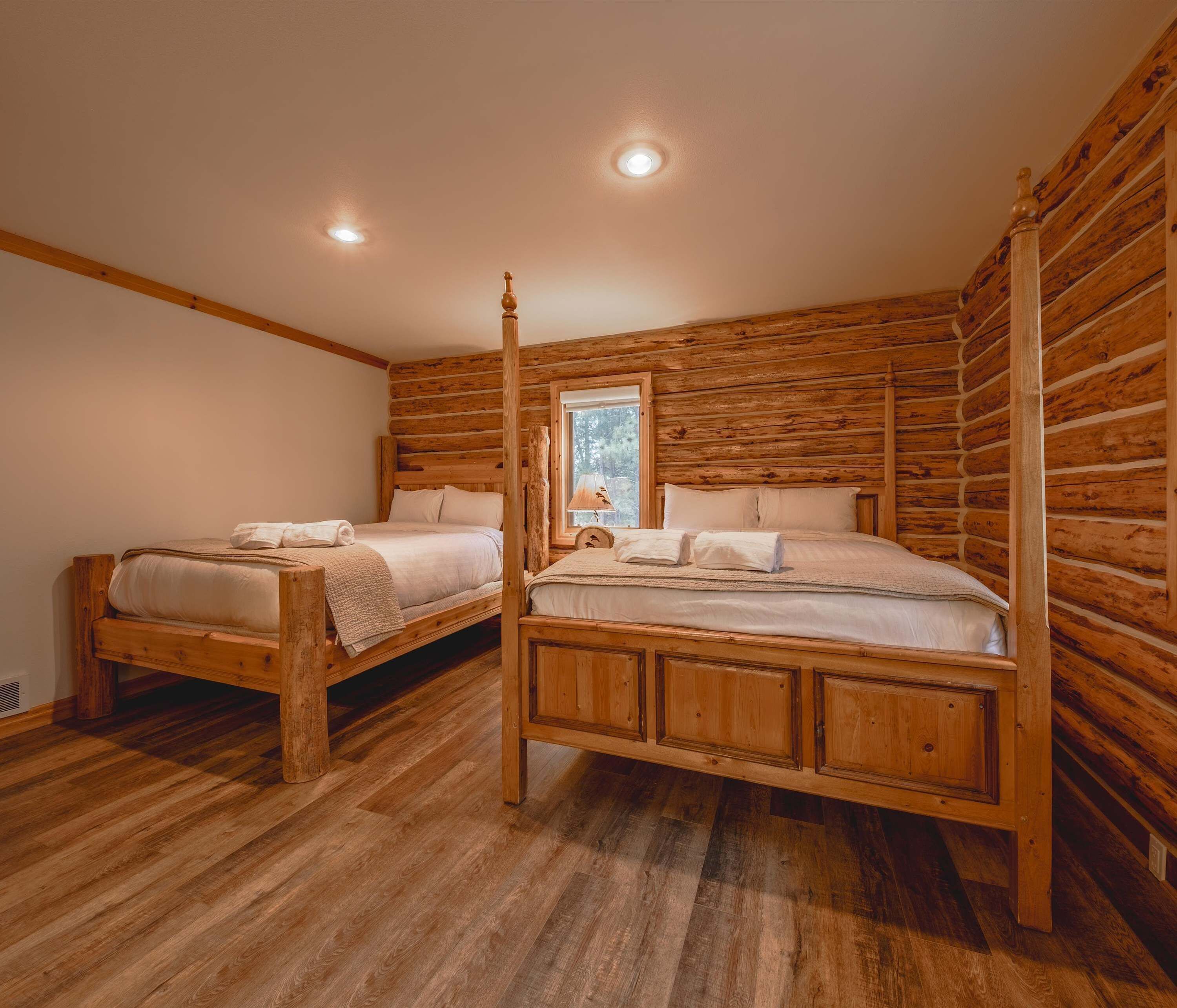 Un dormitorio de estilo cabaña de madera con dos camas de madera, una ventana con vistas y techo de madera.