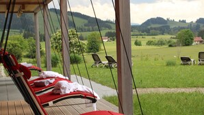 A wooden deck with red lounge chairs and a view of a green landscape. - Sontheims Naturhotel & Spa GmbH&Co.KG (Maierhöfen)