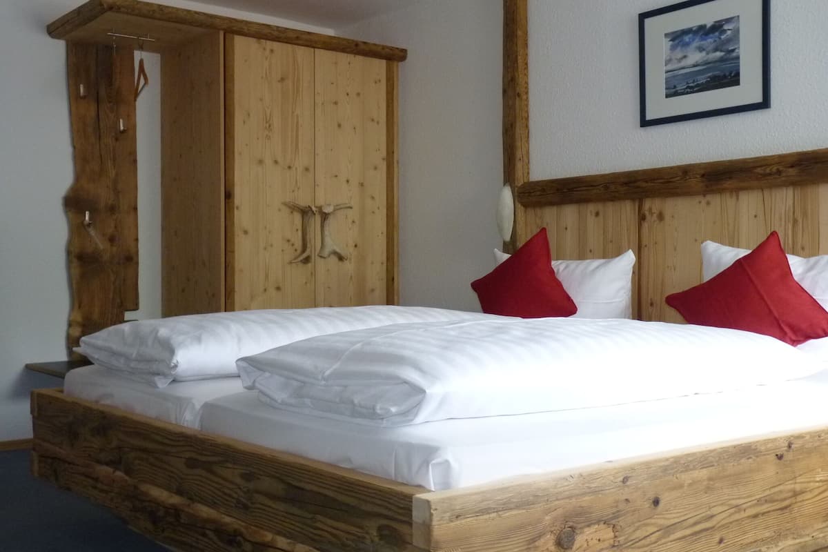 Ein hölzernes Bett mit weißer Bettwäsche und roten Kissen, ein Holzschrank und ein gerahmtes Bild an der Wand.