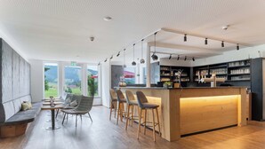 A modern bar area with a wooden counter, bar stools, and a seating area with a sofa and tables. - Sontheims Naturhotel & Spa GmbH&Co.KG (Maierhöfen)